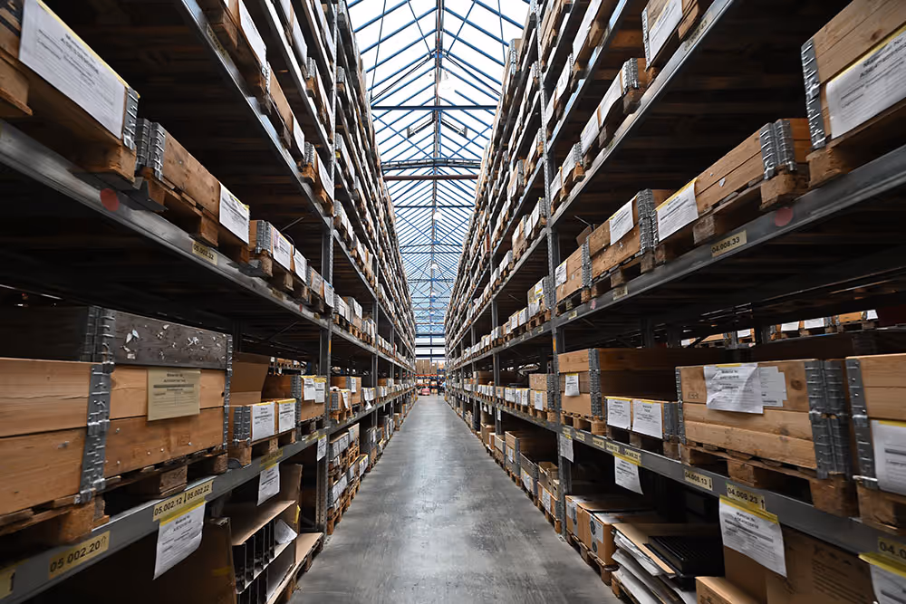 Langer Lagergang mit hohen Regalen voller Holzkisten in einem gut beleuchteten Lagerhaus mit Glasdach.