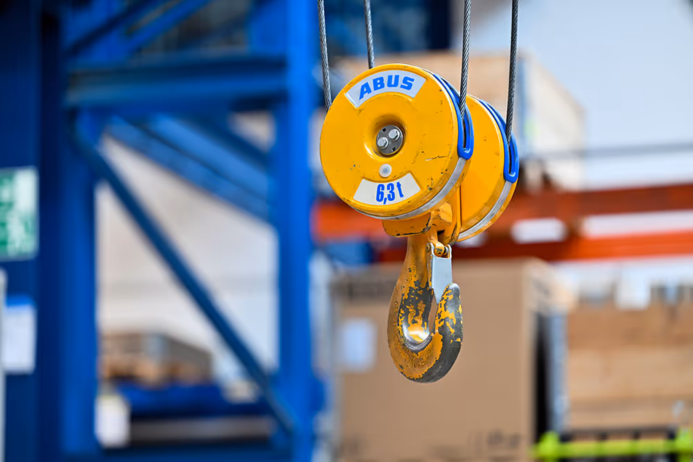 Nahaufnahme eines gelben Kranhakens mit der Aufschrift ABUS und einer Tragfähigkeit von 6,3 Tonnen in einer Lagerhalle.