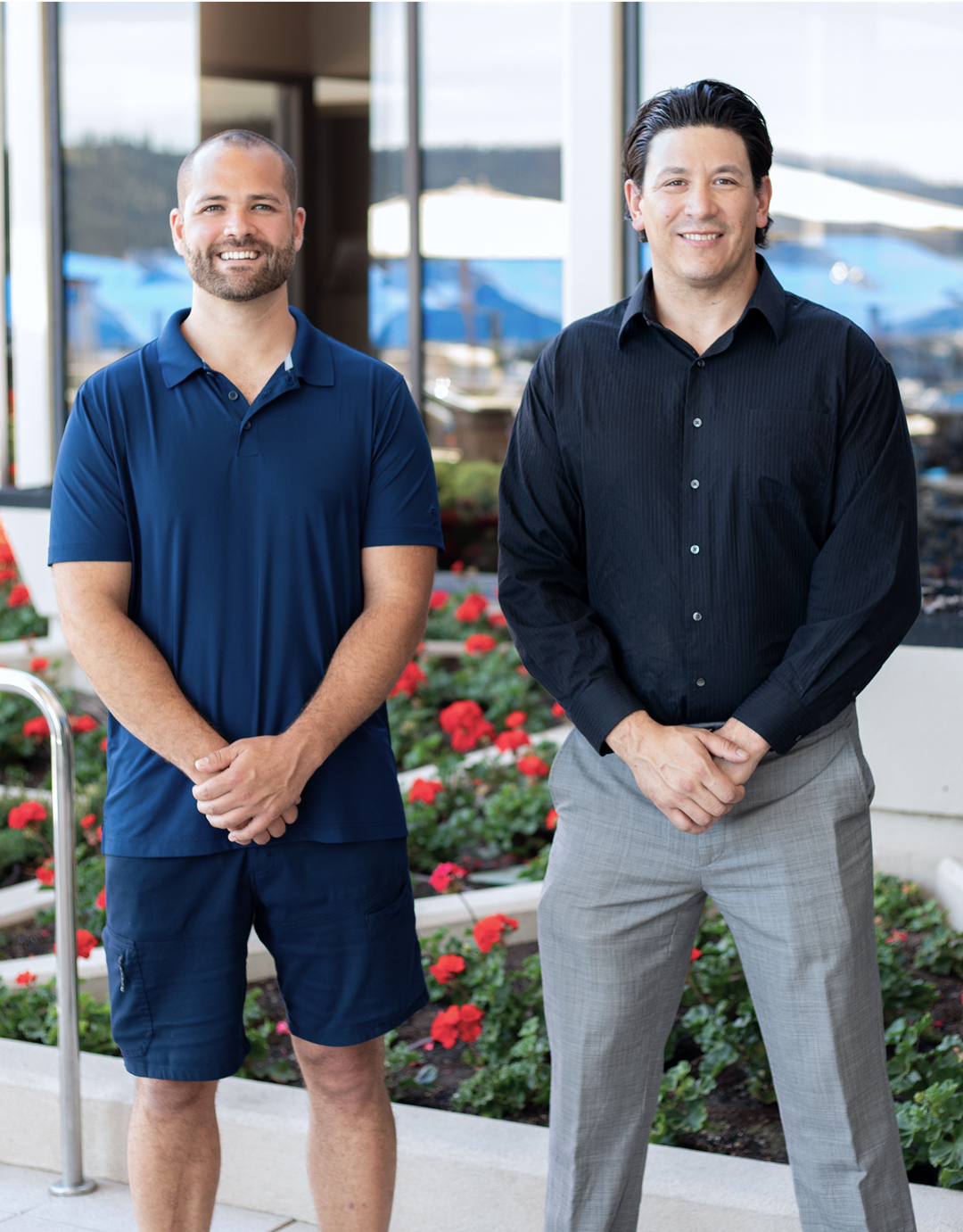 Two smiling colleagues standing together in front of red flower garden