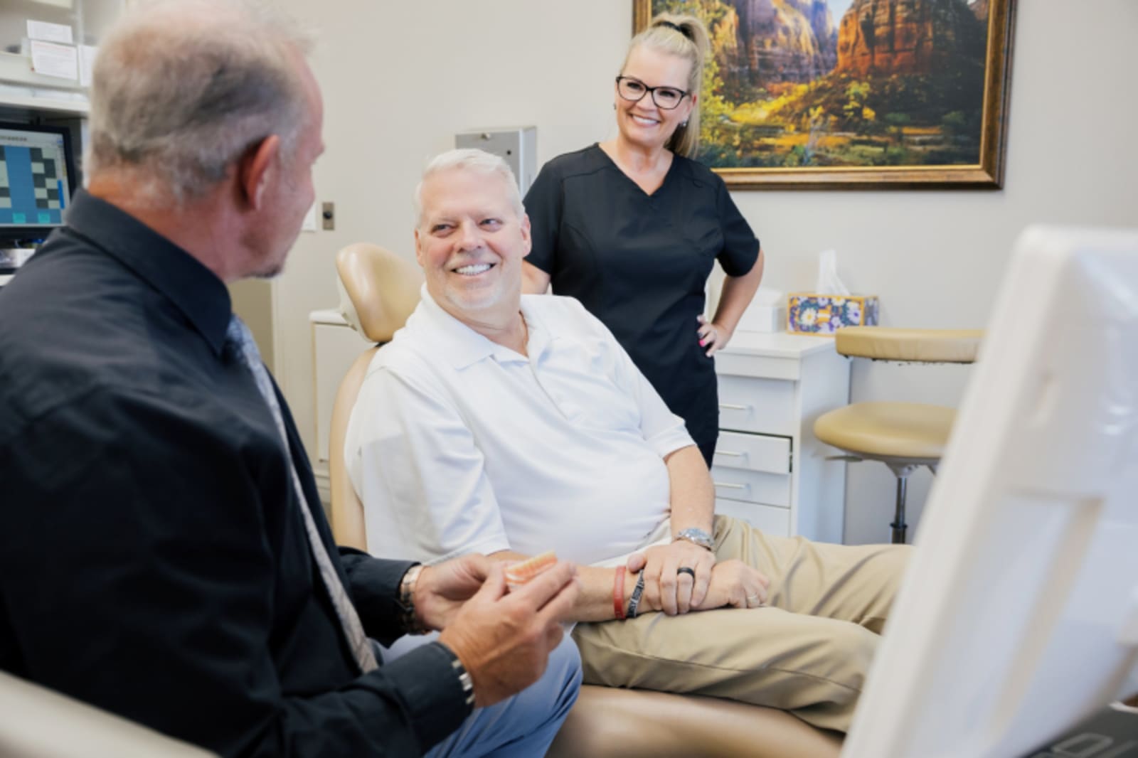 Dentist examining patient in treatment chair with dental professional assisting