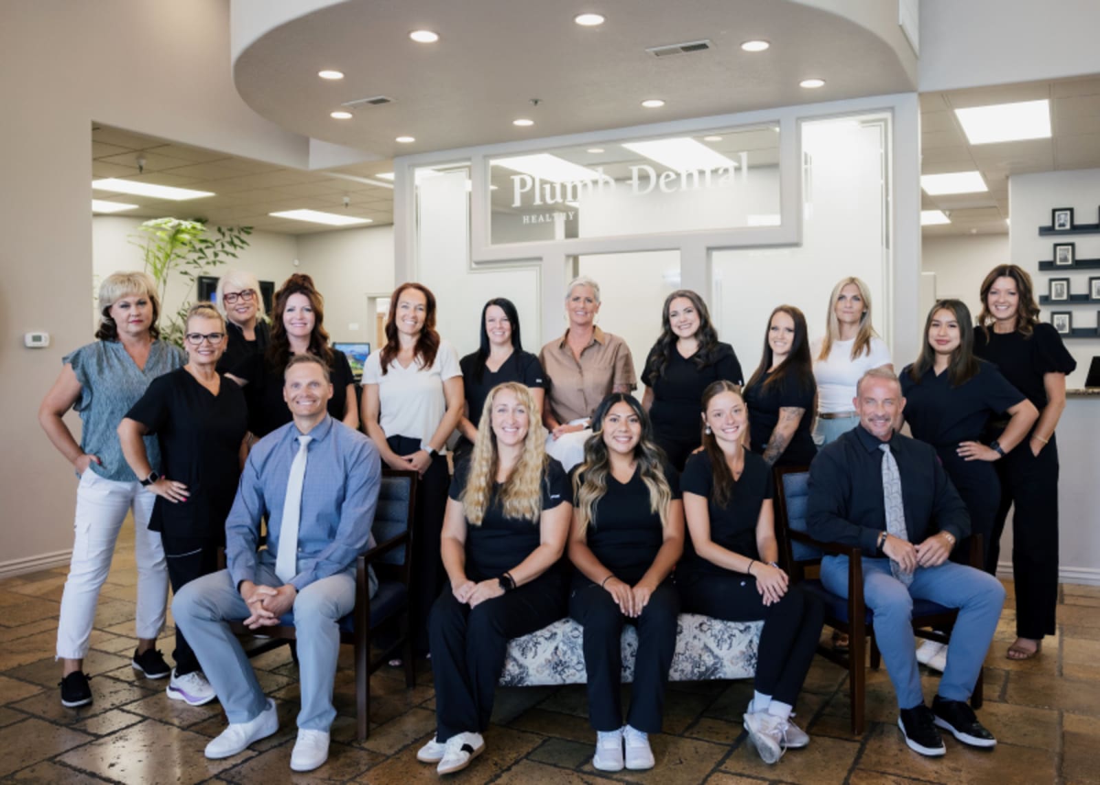 Plumb Dental team members smiling together in a modern dental office reception area.