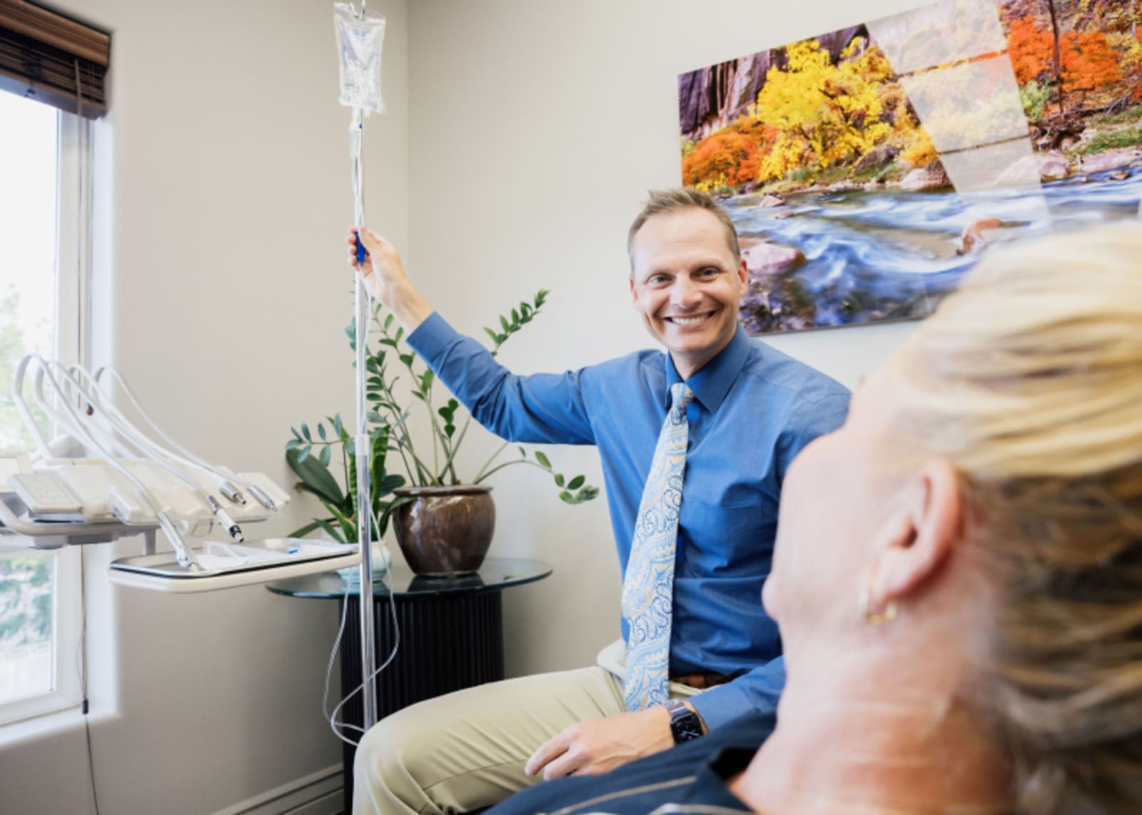 Dentist in blue shirt discussing treatment options with patient in dental office