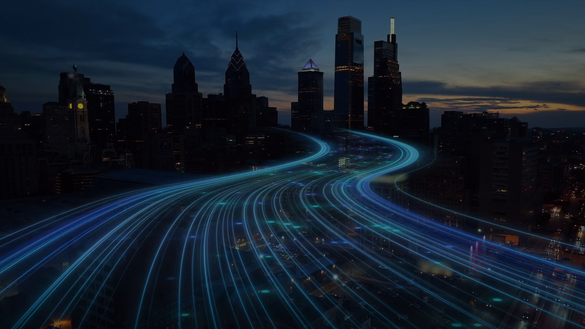City skyline at dusk with light trails representing fast-moving traffic or digital data flows over roads.