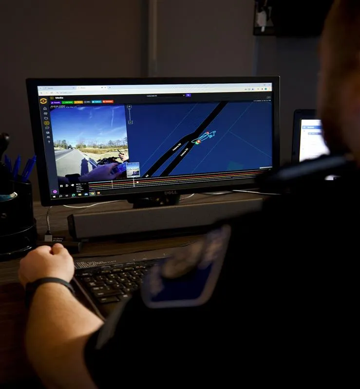 Person wearing a police uniform working on a computer displaying surveillance footage and a map interface.
