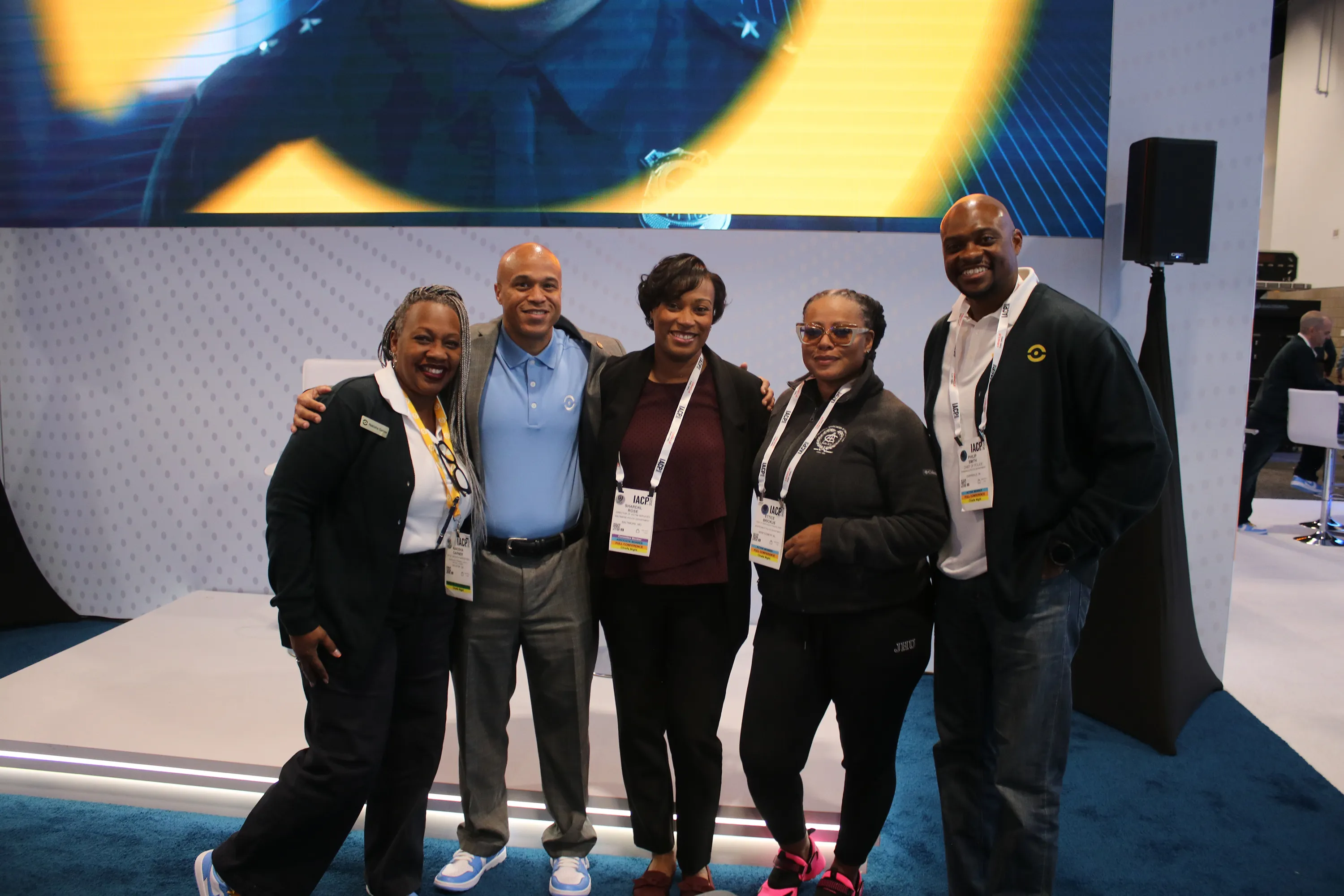 Group of five people standing together at a conference, smiling and wearing name badges with lanyards.