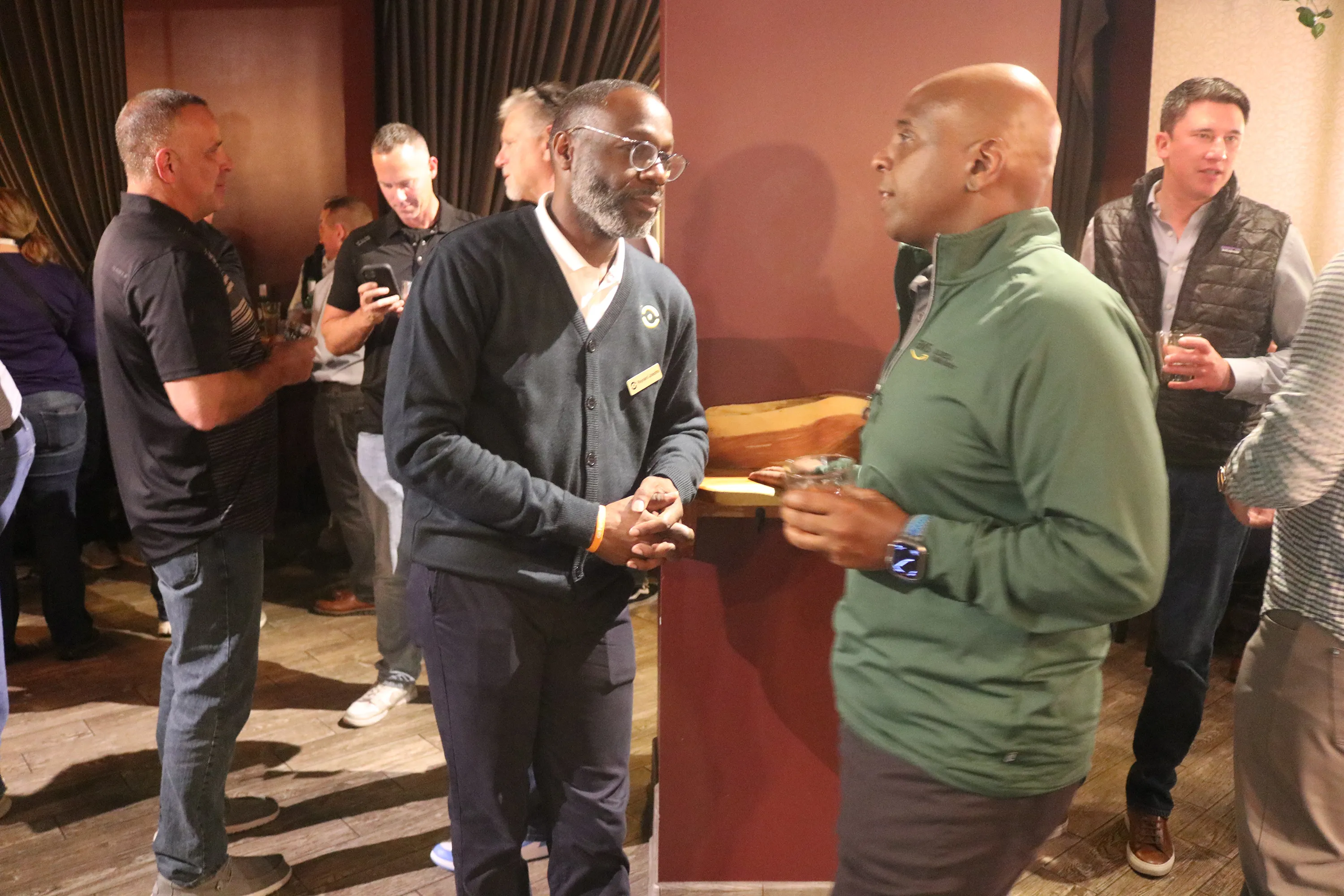 Several men engaged in conversation at an indoor social event, some holding drinks.