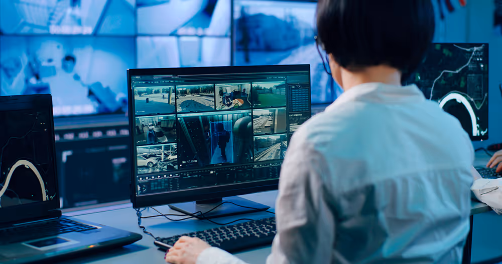Person monitoring multiple surveillance camera feeds on a computer screen in a control room.