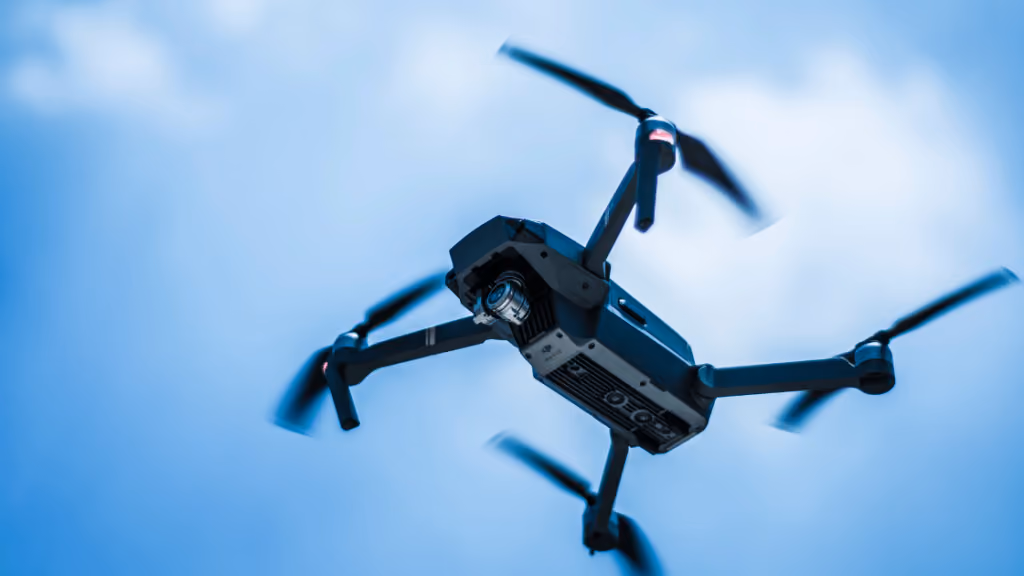 Close-up of a quadcopter drone flying against a bright blue sky with blurred propellers.