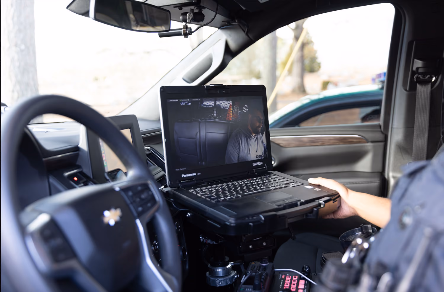 Police vehicle interior with a laptop showing camera footage of a person in the back seat.