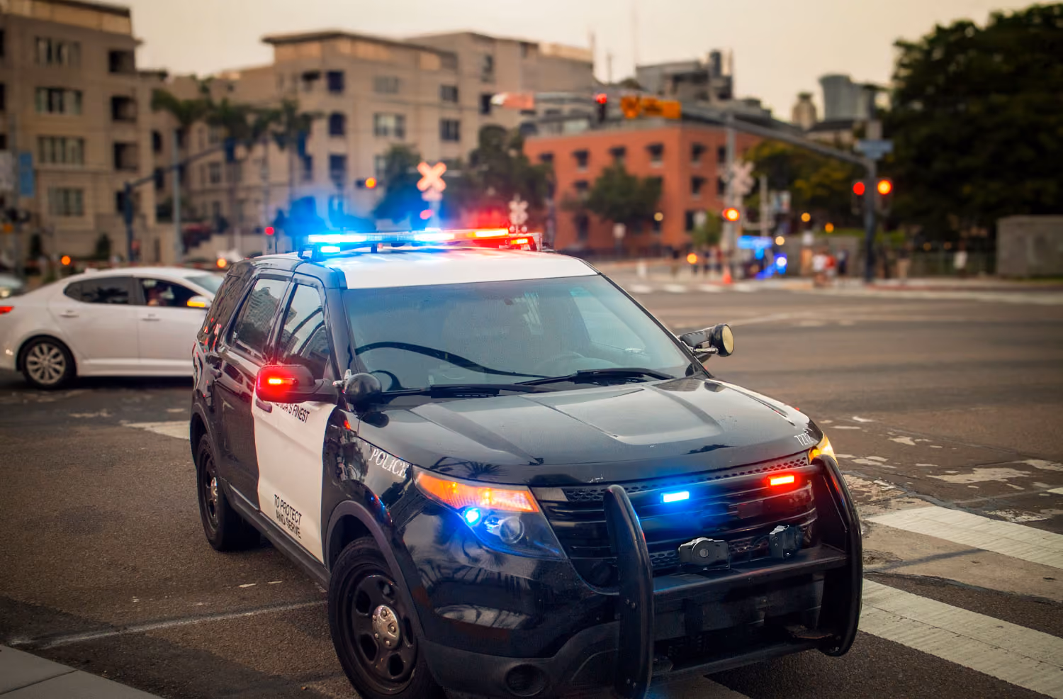 Black and white police SUV with flashing red and blue lights parked on a city street intersection.