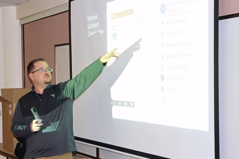 Man in glasses pointing at a projection screen with a remote in his hand during a presentation.