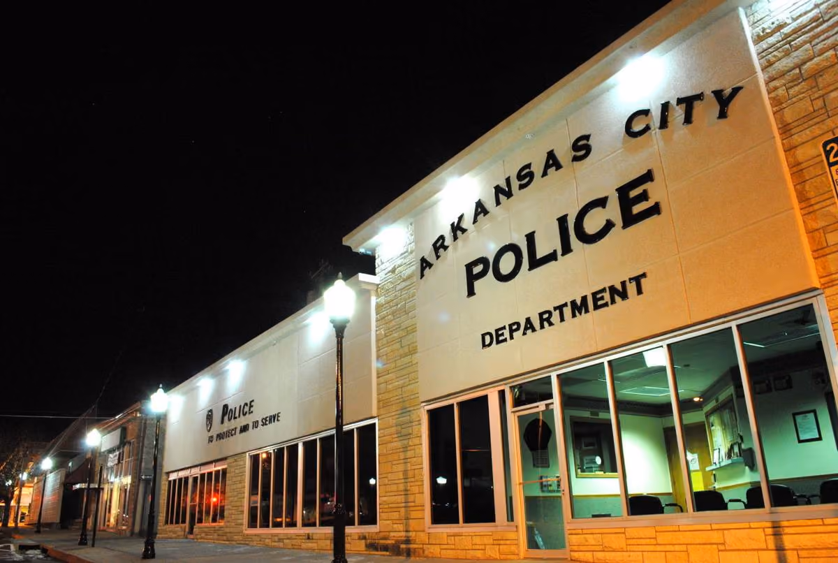 Night view of Arkansas City Police Department building lit with street lamps and interior lights.