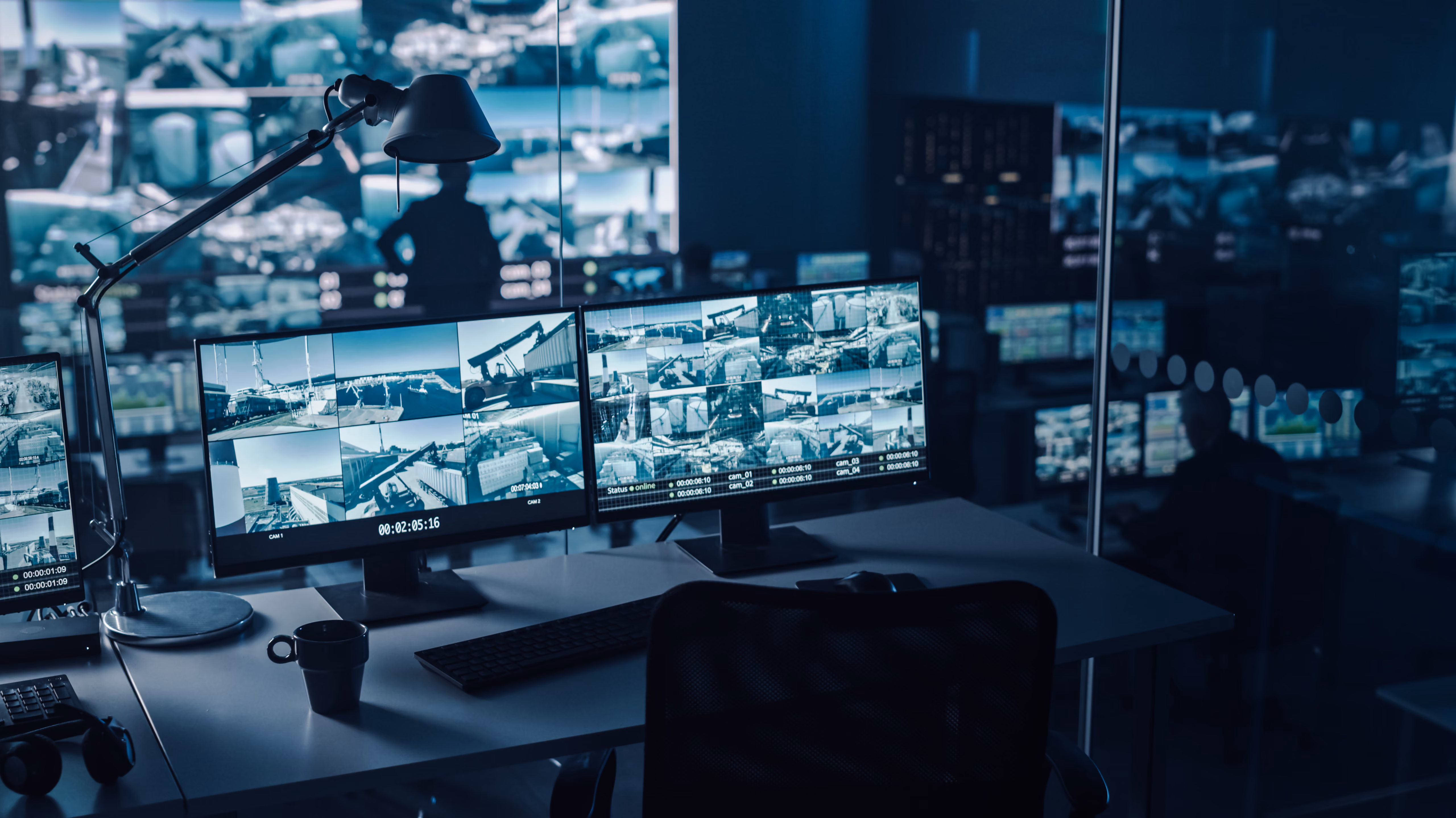 Desk with multiple surveillance monitors showing security camera feeds in a dark monitoring room.