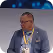 Man wearing glasses and a blue shirt with a conference lanyard against a blue background.