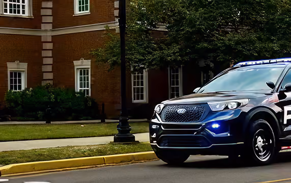 Front side of a police SUV with lights on parked near a brick building and a street lamp.