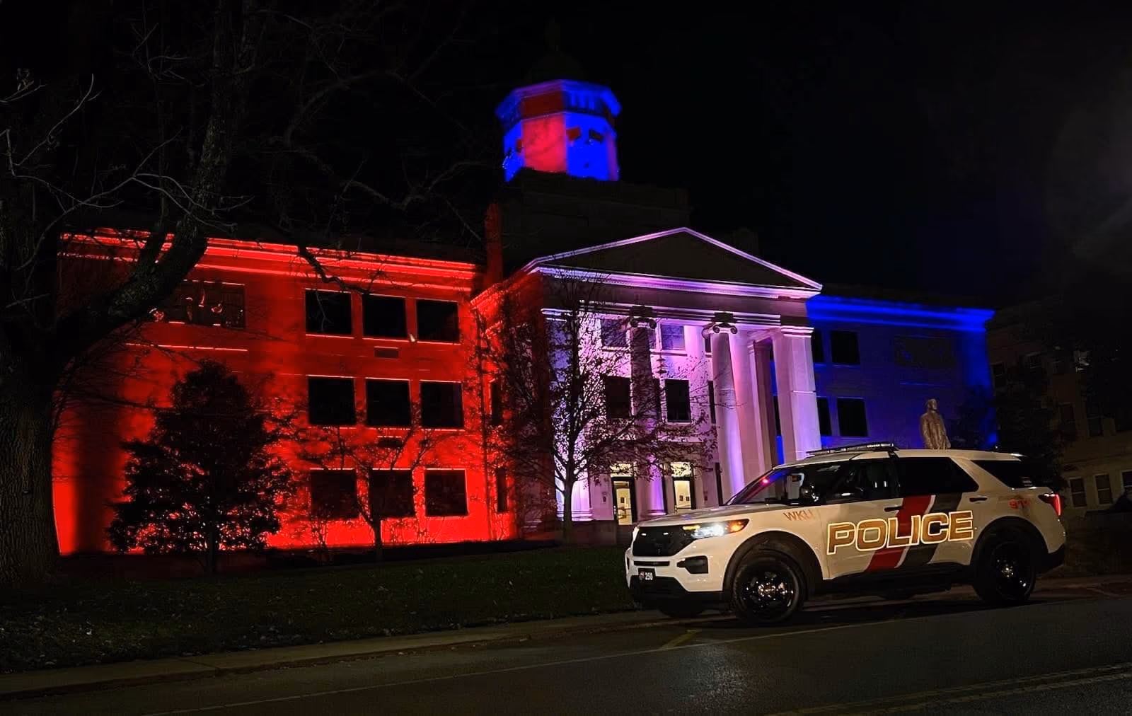 Police SUV parked in front of a building lit with red, white, and blue lights at night.
