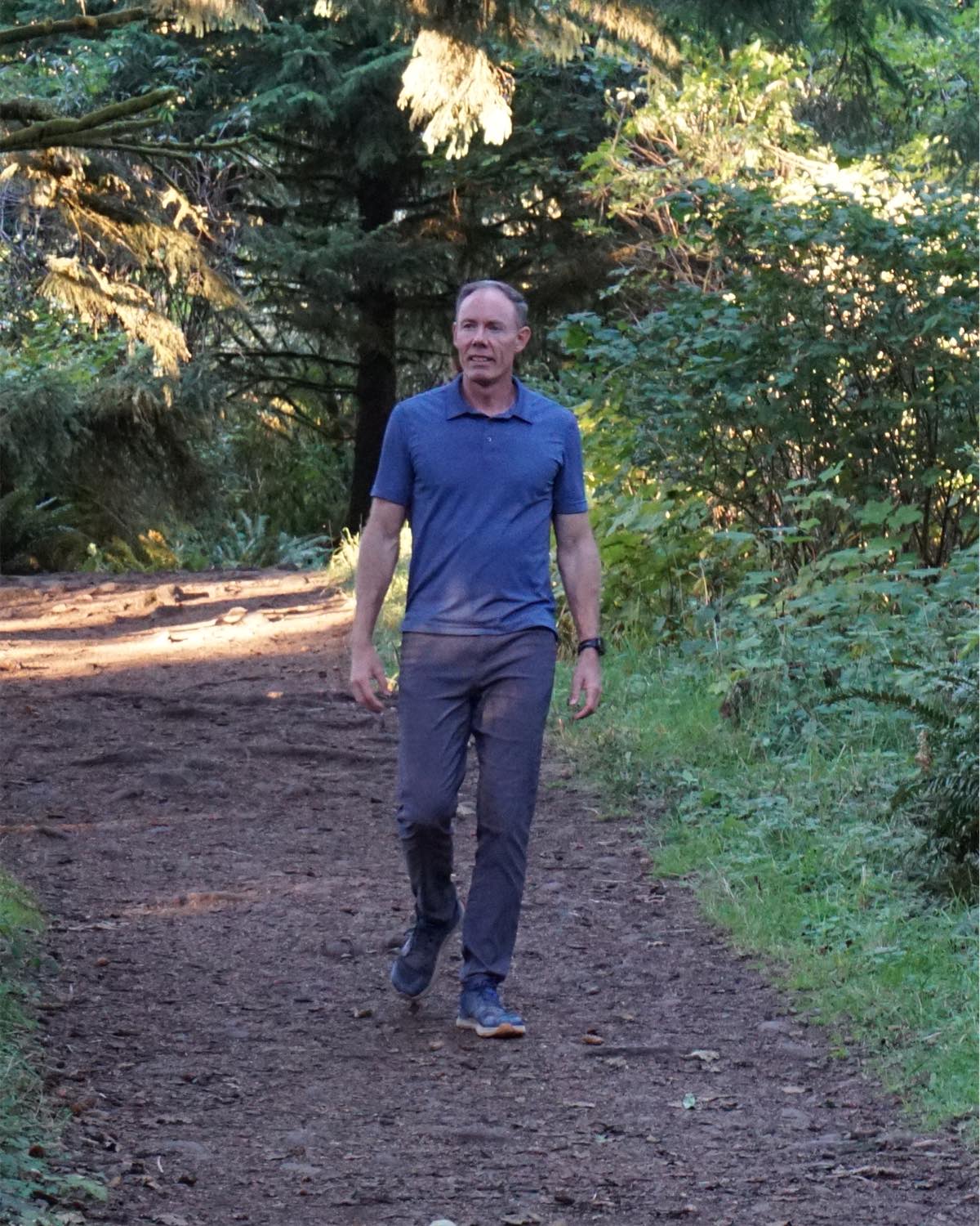 Greg Burnham walking along a sunlit forest trail in Oregon.