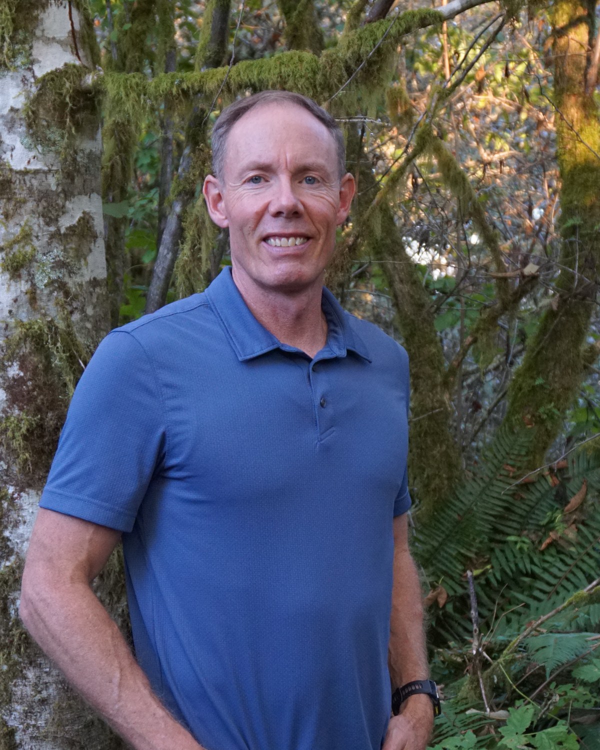 Greg Burnham smiling beside a birch tree in an Oregon forest.