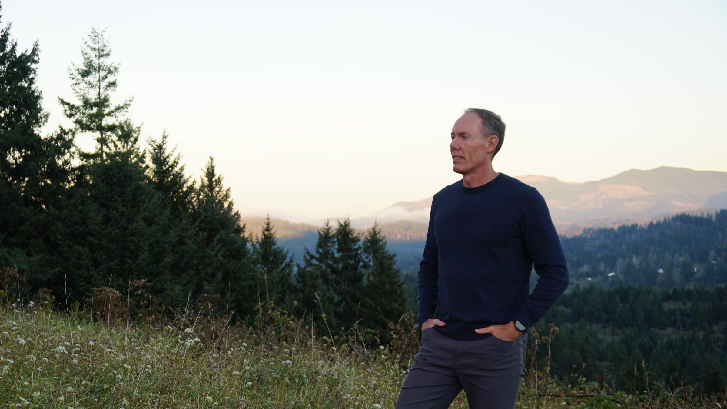 Greg Burnham standing on a hillside at sunset, looking out over Oregon hills.