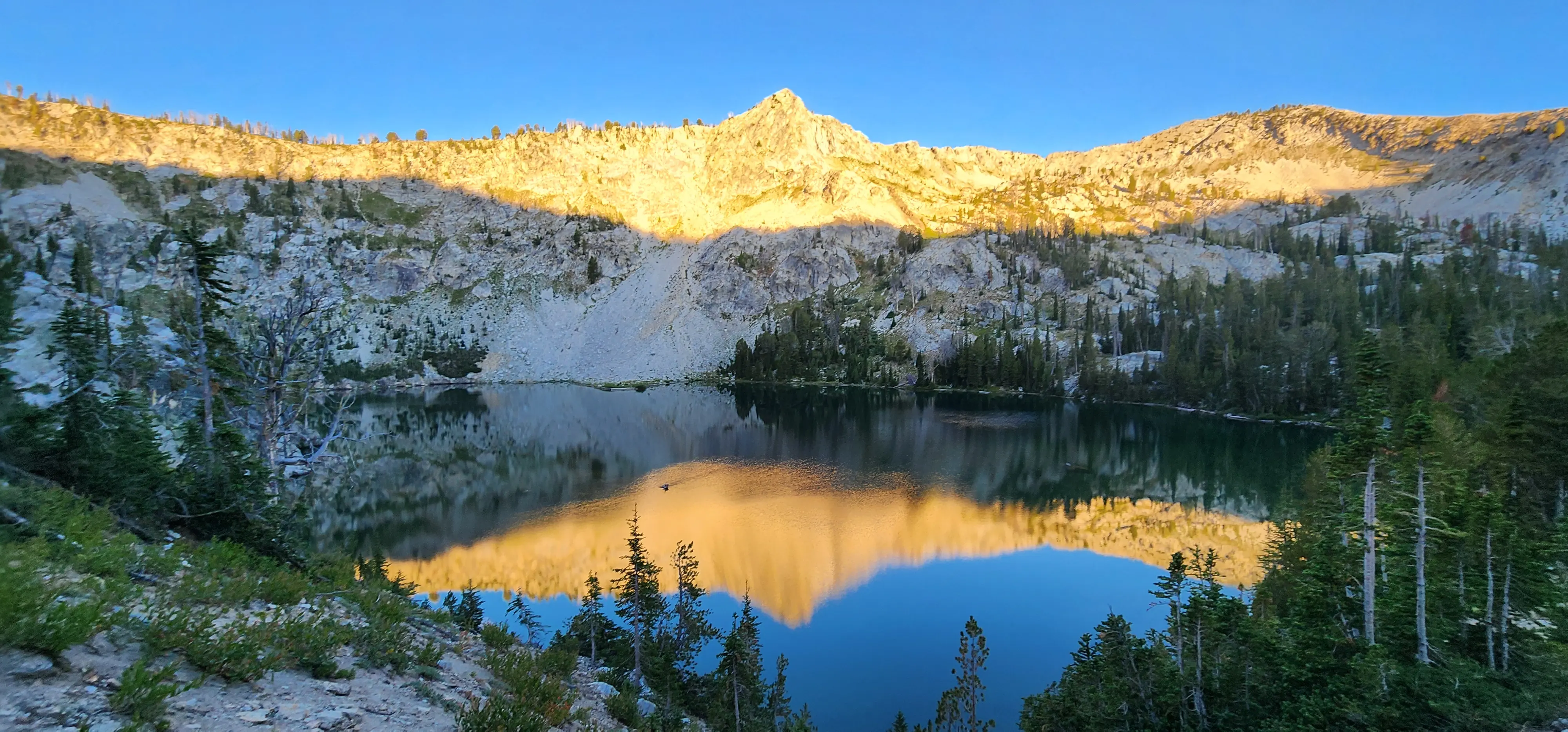 Alpine lake at sunrise below a granite ridge in the Idaho mountains