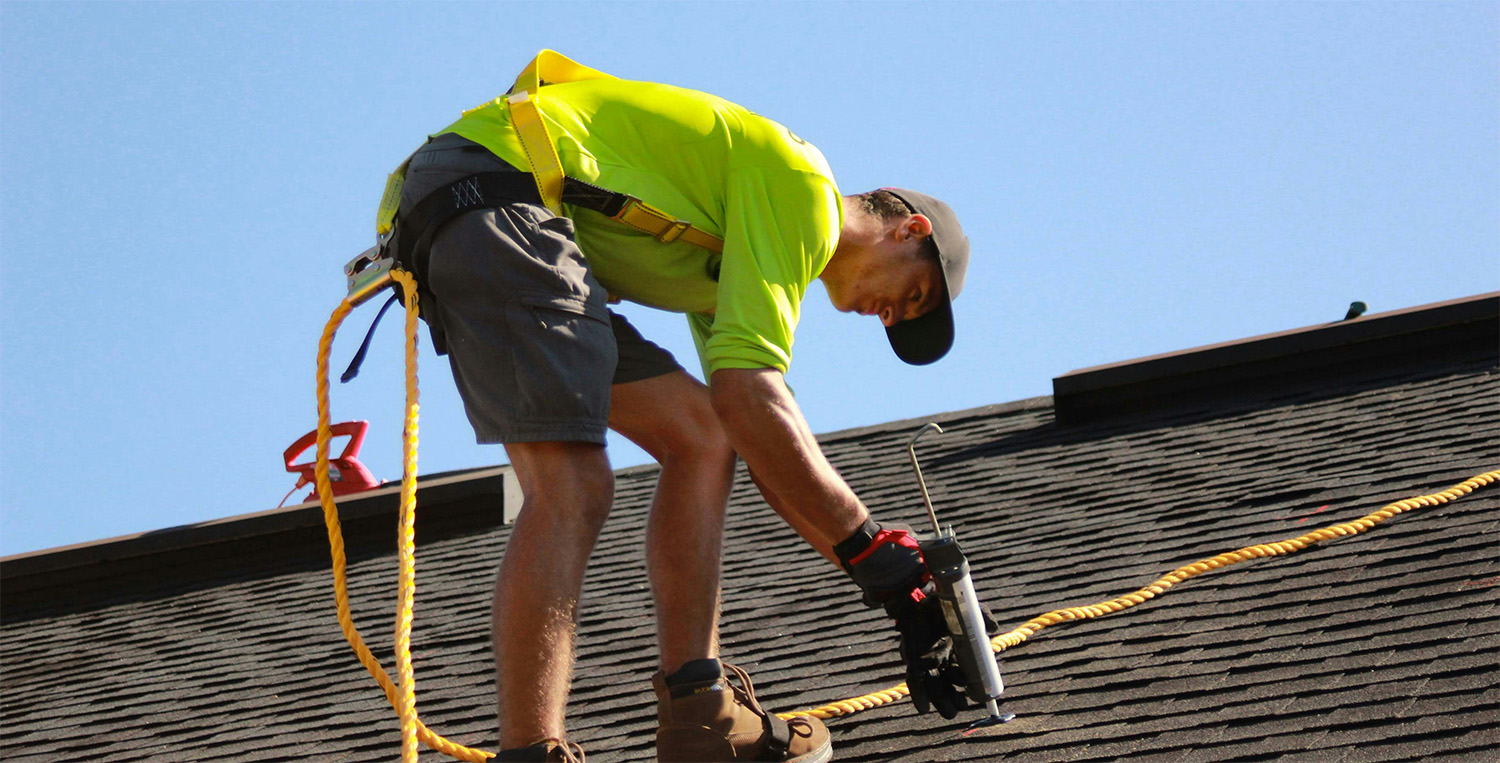 Roofer in safety gear using a nail gun to install shingles on a roof in Spokane W