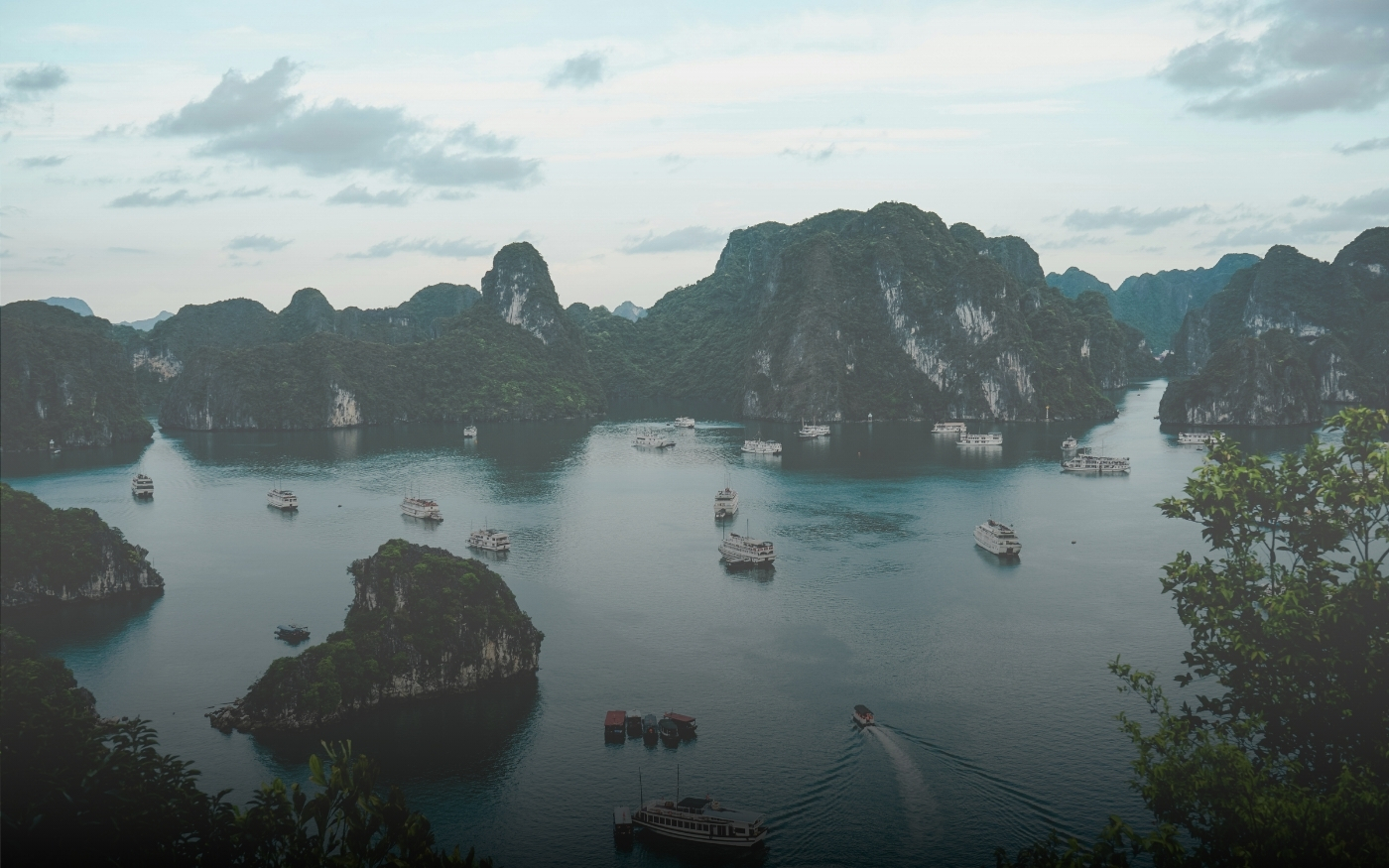 Panorámica de bahía con numerosas formaciones rocosas cubiertas de vegetación y varios barcos navegando en aguas tranquilas bajo un cielo nublado.