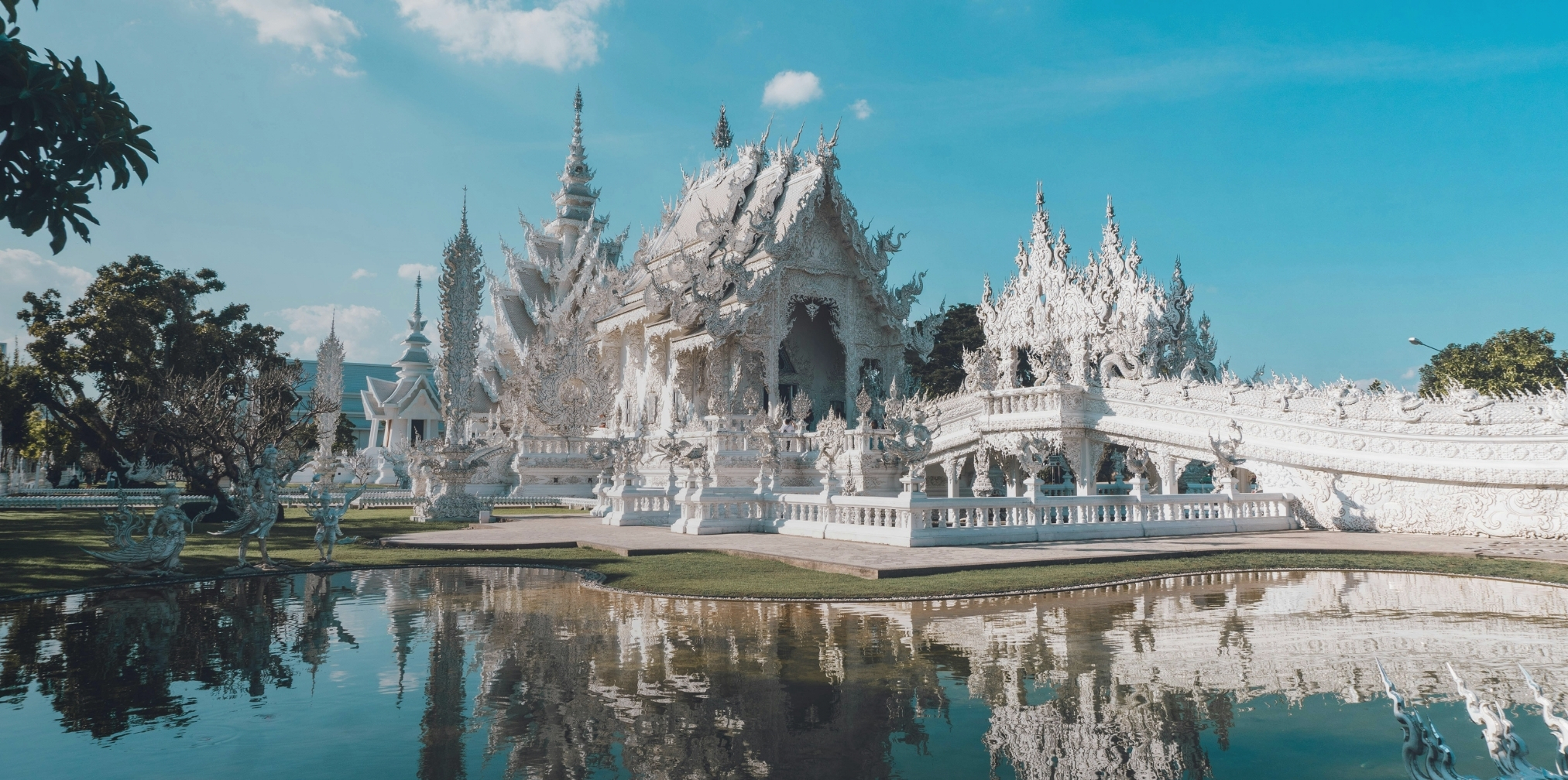 Templo blanco ornamentado con reflejo en un estanque bajo un cielo azul despejado.