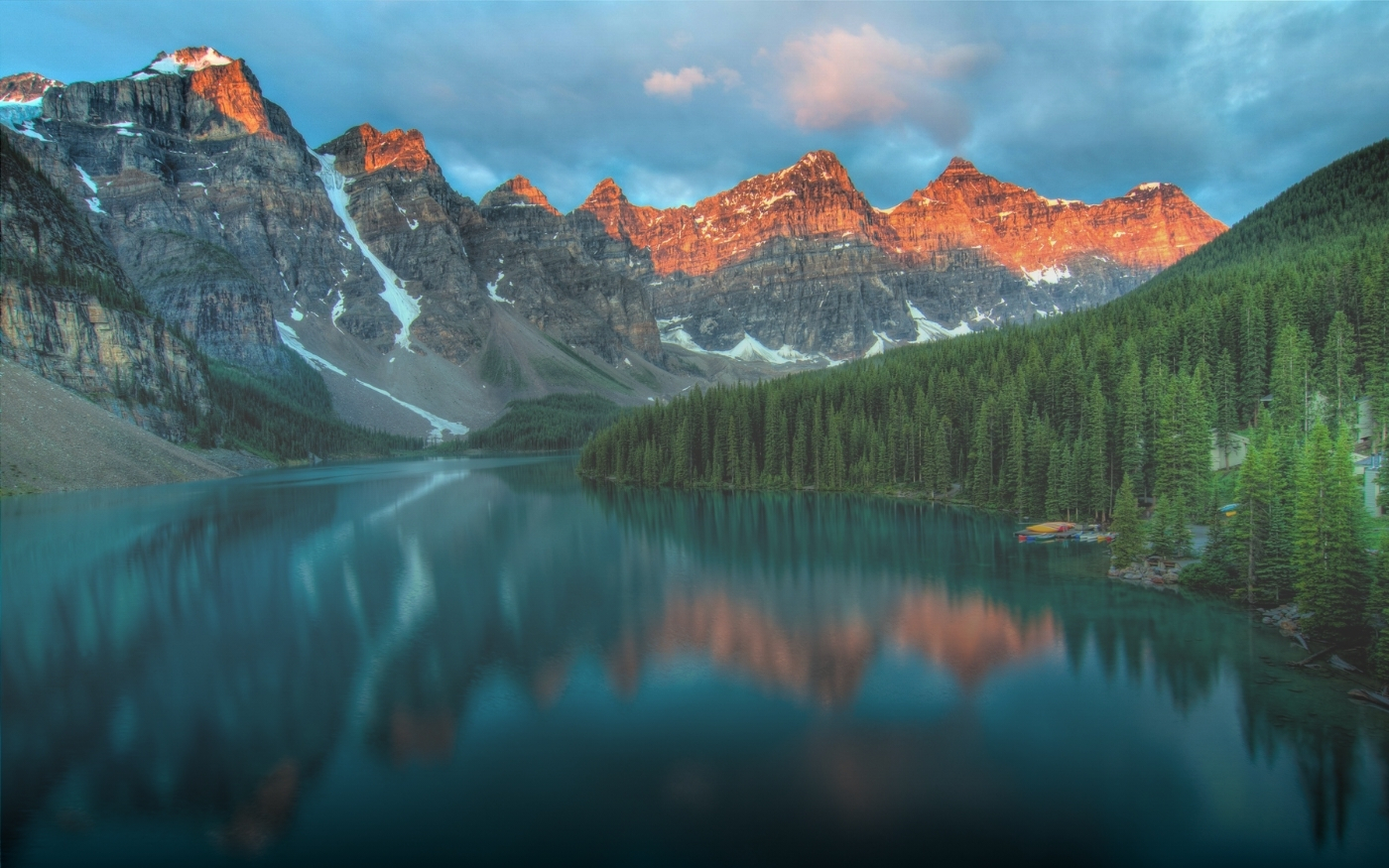 Lago rodeado de bosque y montañas rocosas iluminadas por la luz dorada del atardecer.