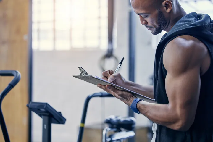 A man writing on a clipboard in a gym.