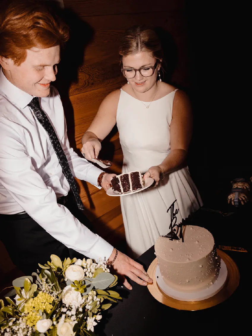 Bride and groom cutting and serving a slice of chocolate layered wedding cake.