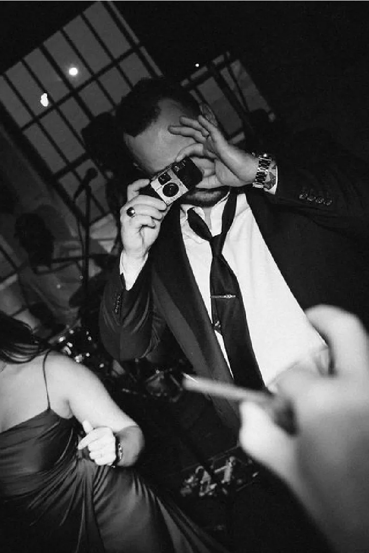 Man in a suit taking a photo with a vintage camera at a nighttime event.