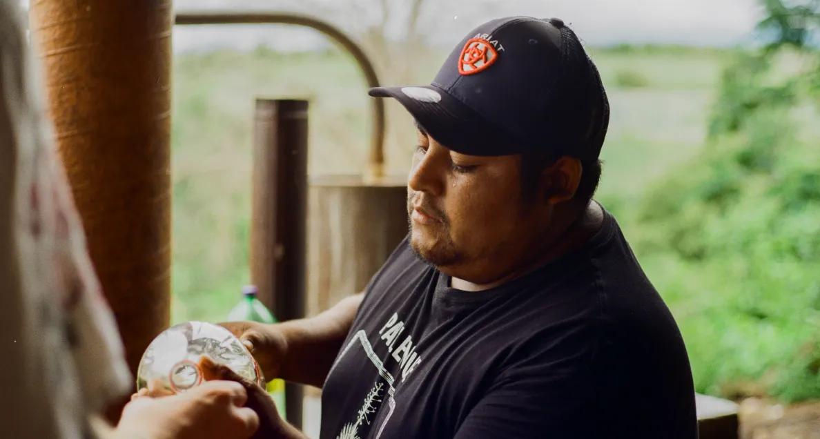 Man wearing a black Ariat cap and a black shirt holding a wrapped item outdoors.