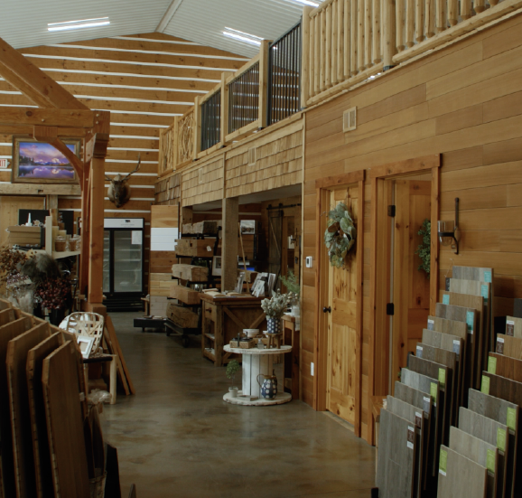 Interior of a wooden showroom with flooring samples and rustic furniture displays.
