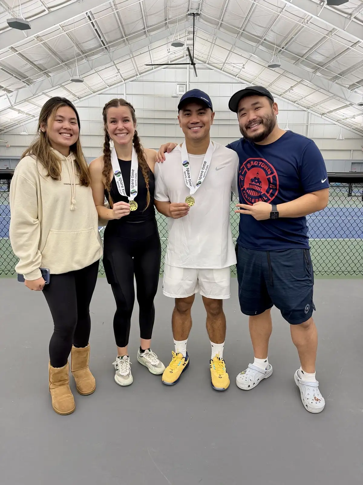 Four people smiling indoors on a sports court, two in the center wearing medals and sportswear.
