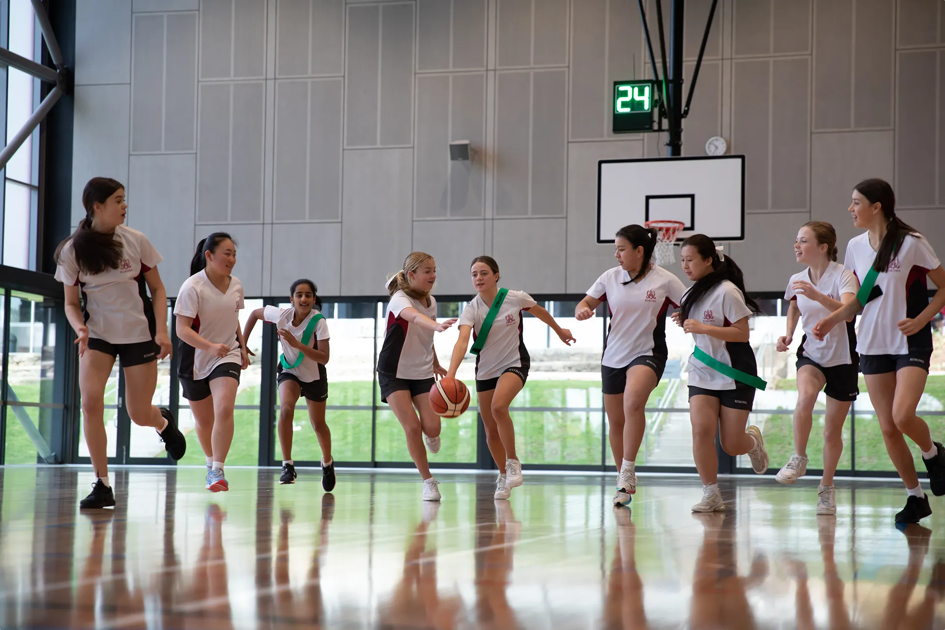 Group of girls playing basketball indoors, one girl dribbling the ball while others run around her.