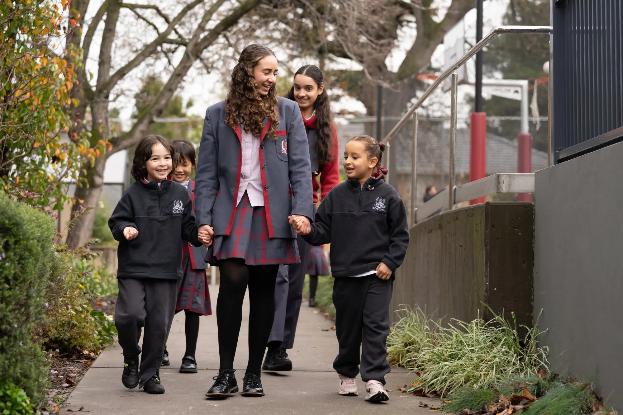 Group of smiling school children in uniforms walking together on a sidewalk outdoors.