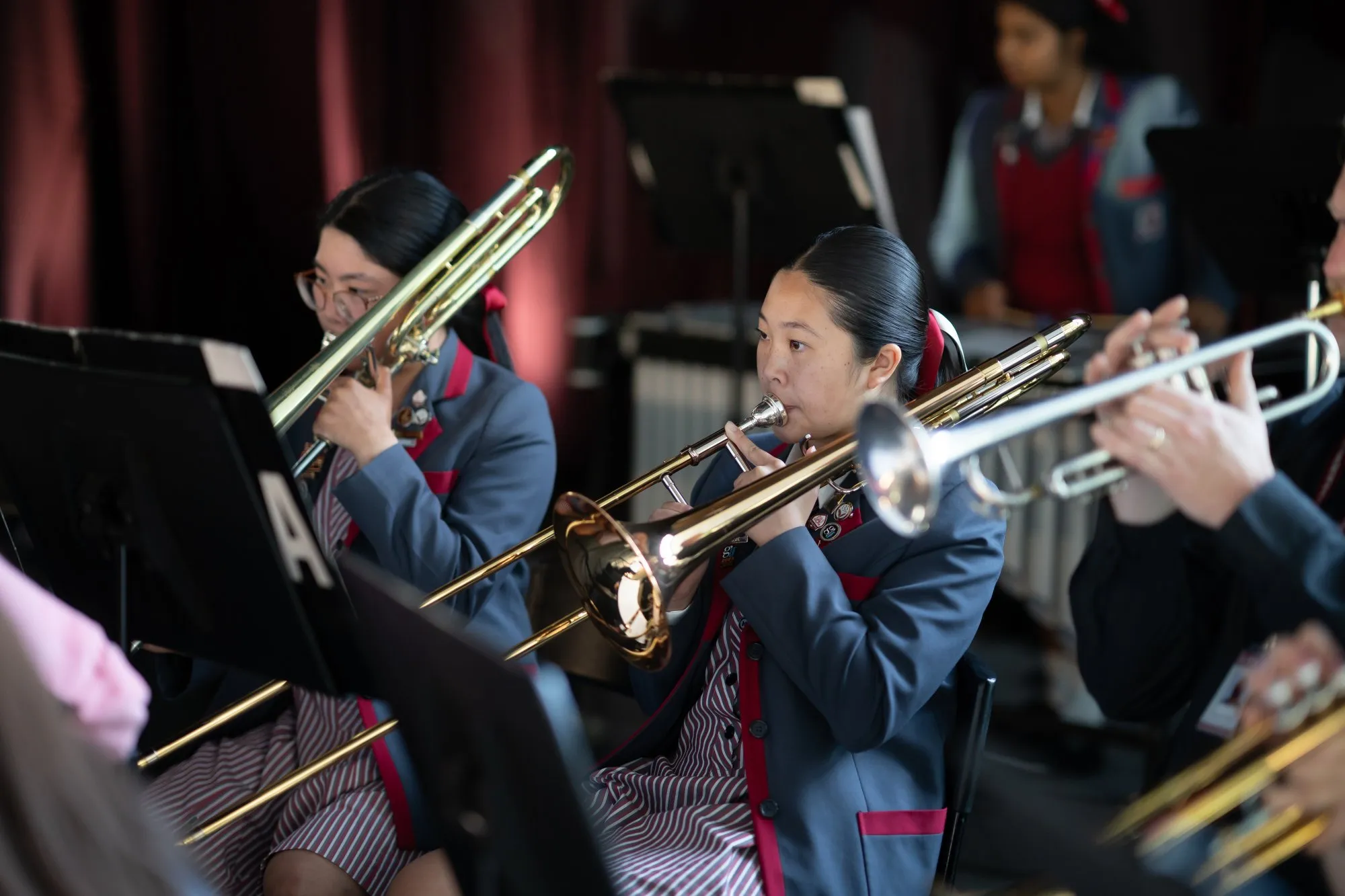 Two young female musicians in school uniforms playing trombones during a band performance.