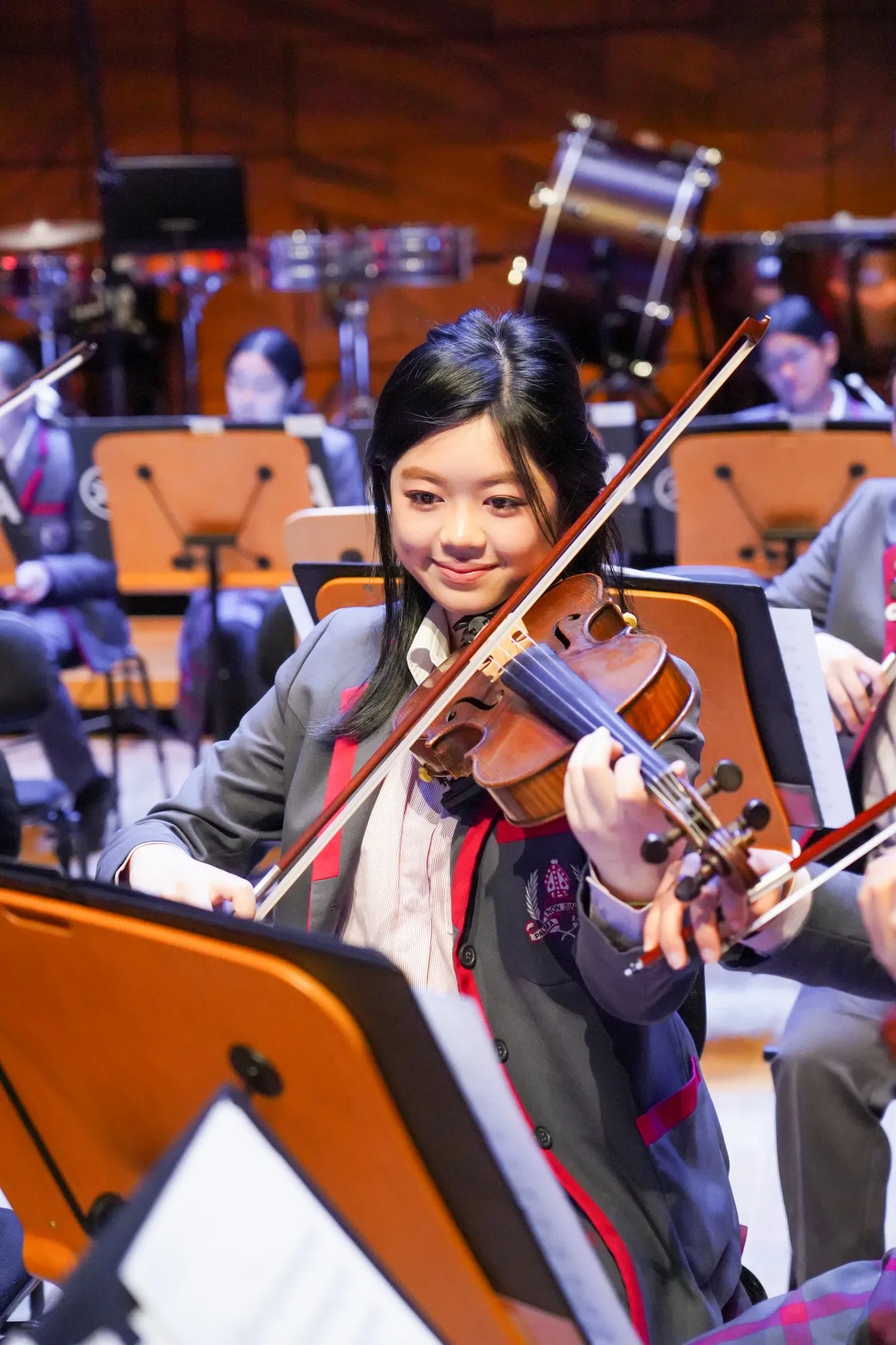 Young female violinist in uniform playing violin in an orchestra setting.