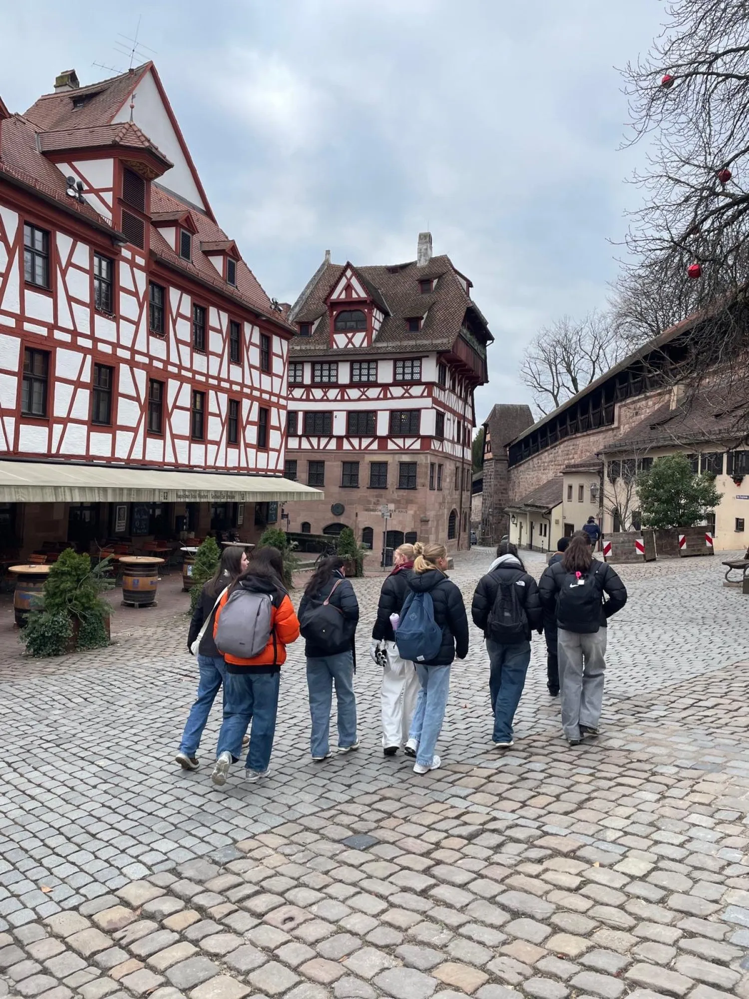 Group of seven people walking on a cobblestone street past traditional half-timbered buildings under a cloudy sky.