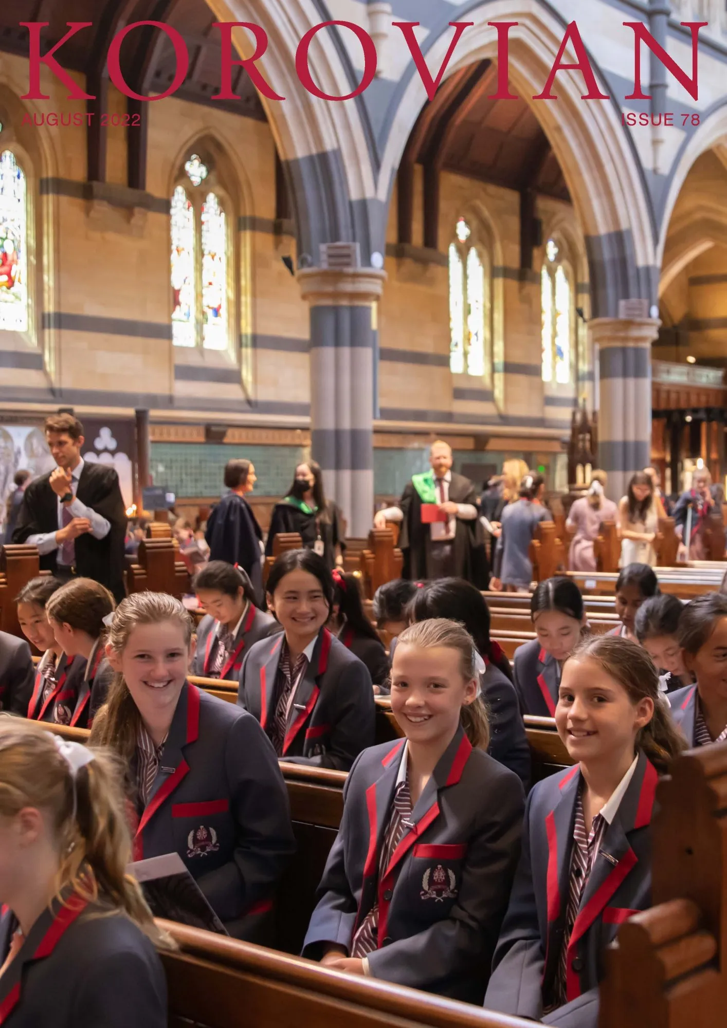 Students in school uniforms sitting and smiling inside a church with stained glass windows and large arches.
