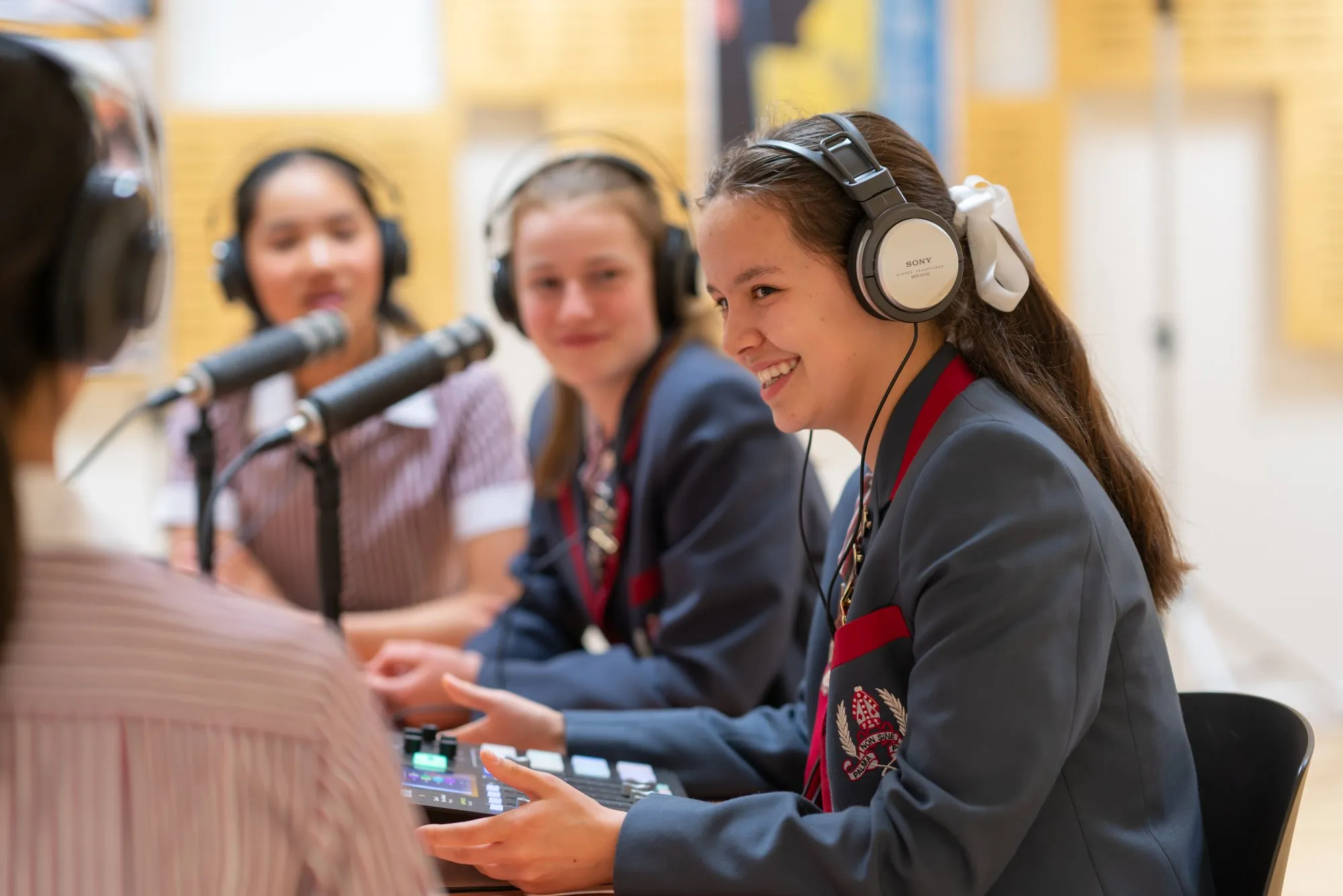 Three female students in school uniforms wearing headphones and talking into microphones during a recording session.