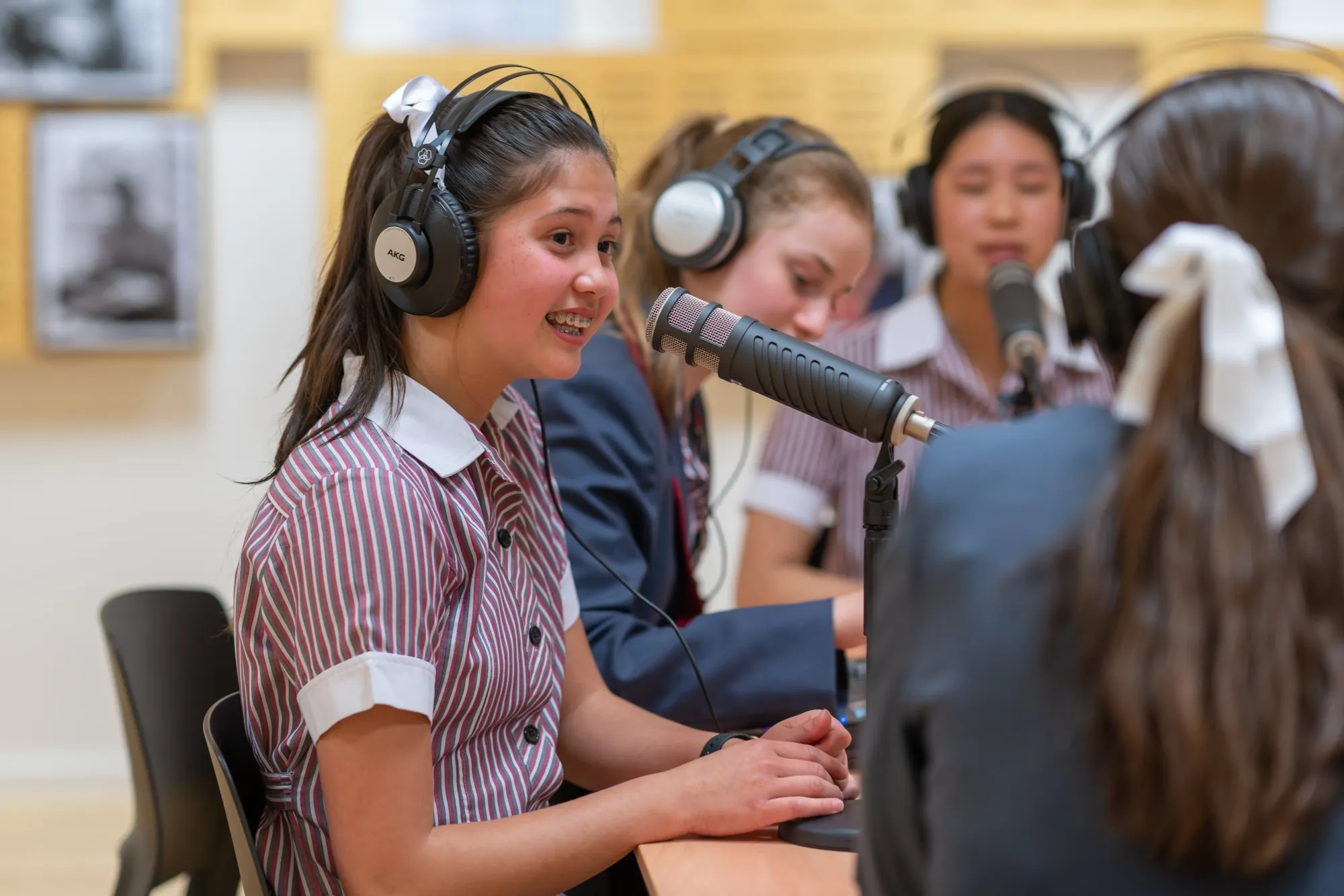 Teen girls wearing headphones and speaking into microphones in a recording studio or radio broadcast setting.