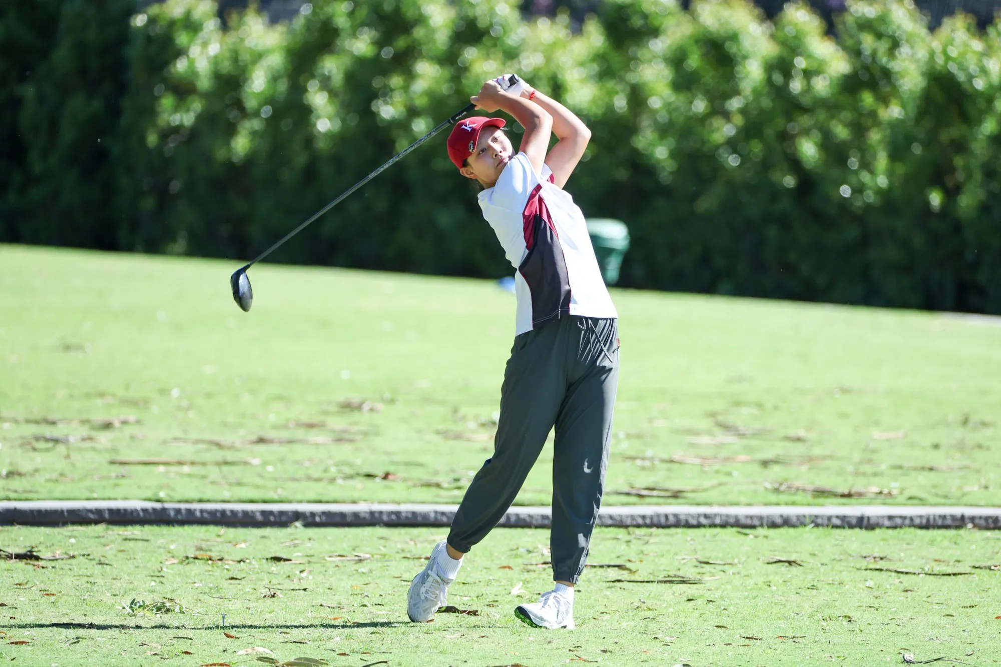 Golfer in a red cap and white shirt swinging a golf club on a grassy course.