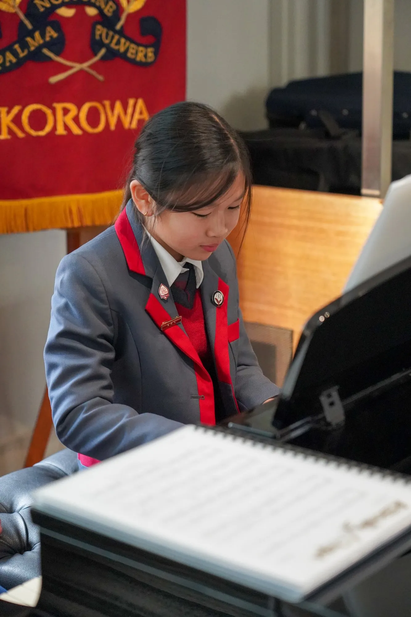Young girl in school uniform playing a grand piano with sheet music in front of her.