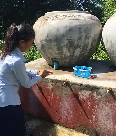 Woman washing her hands at an outdoor water station with large ceramic water jars.