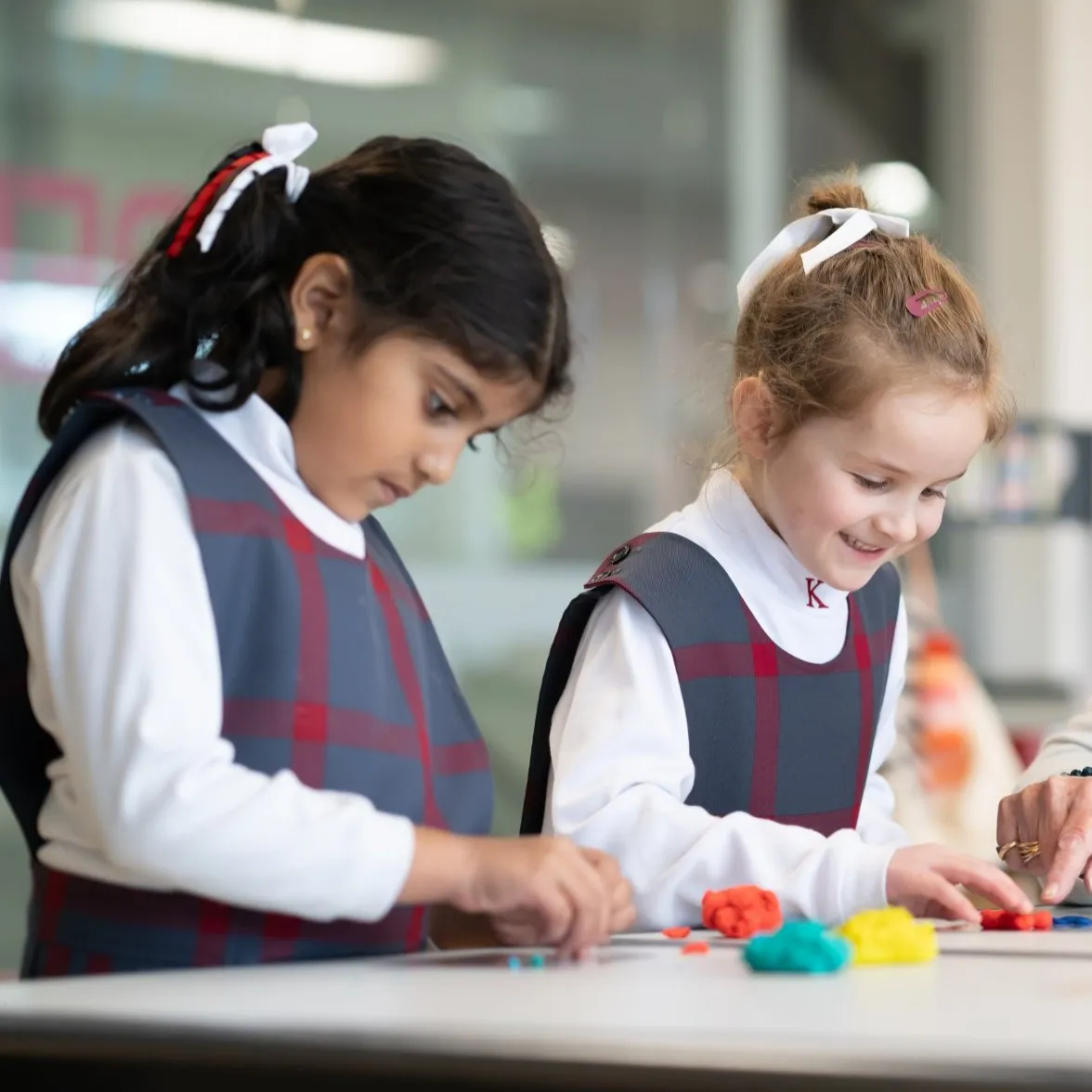Two young girls in school uniforms playing and molding colorful clay at a table.