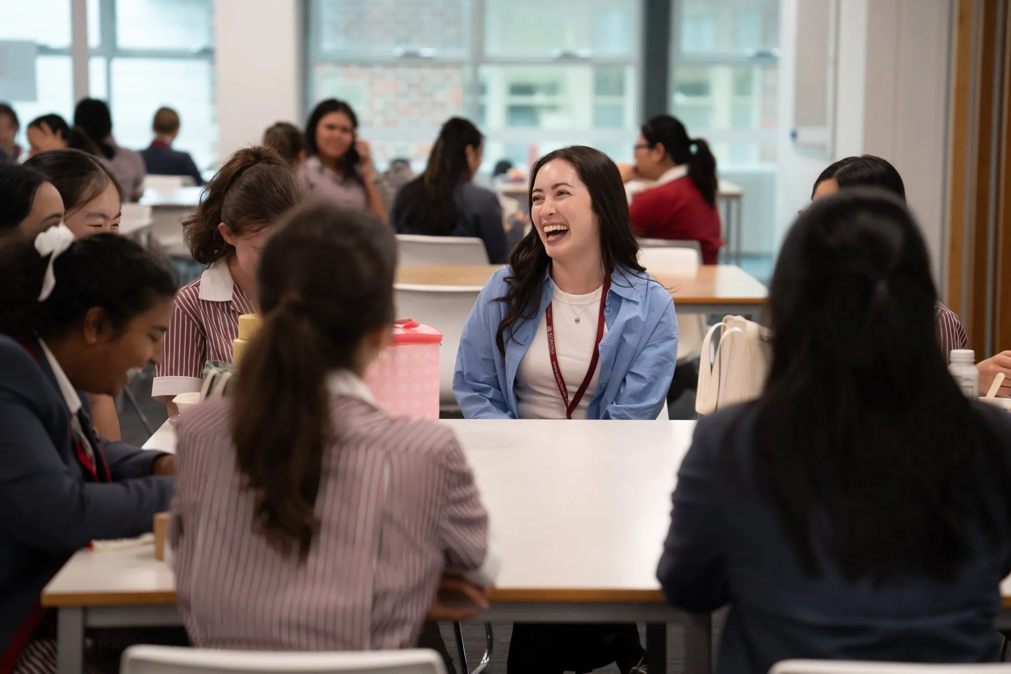 A group of students sitting around a table in a classroom, with one student in a blue jacket laughing.