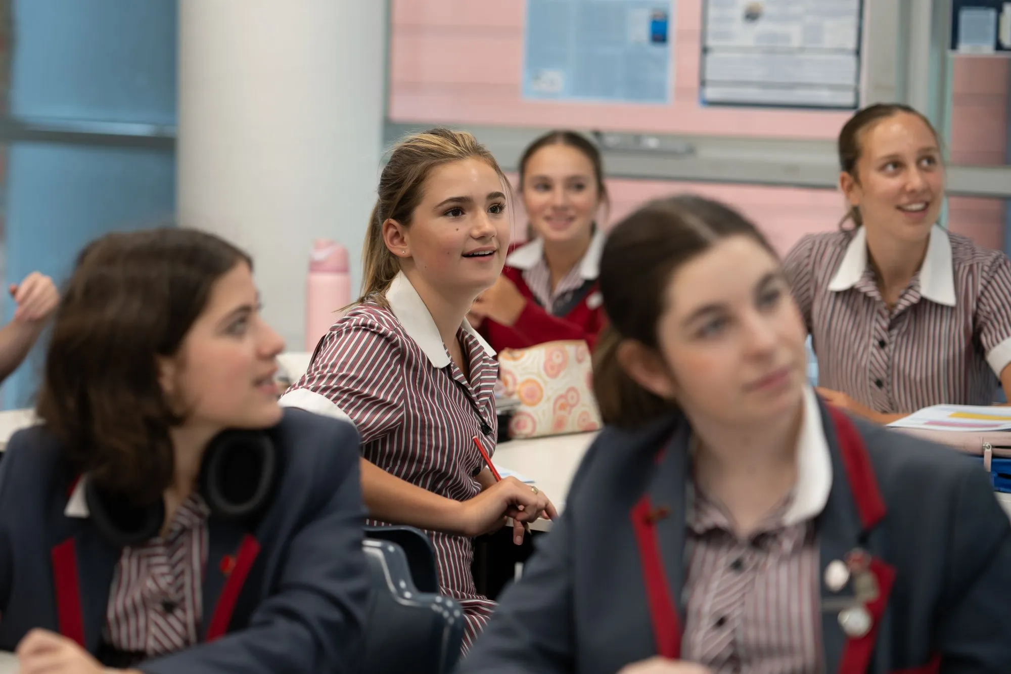 Group of female students in striped uniforms attentively listening in a classroom.