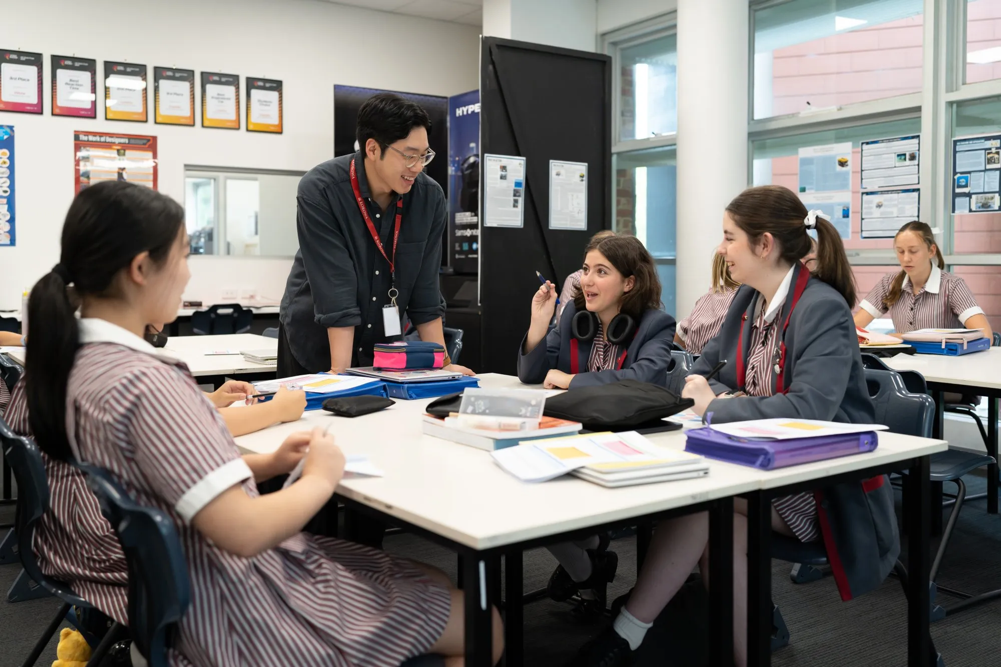 Teacher engaging with high school students in uniforms sitting around a classroom table with books and notebooks.