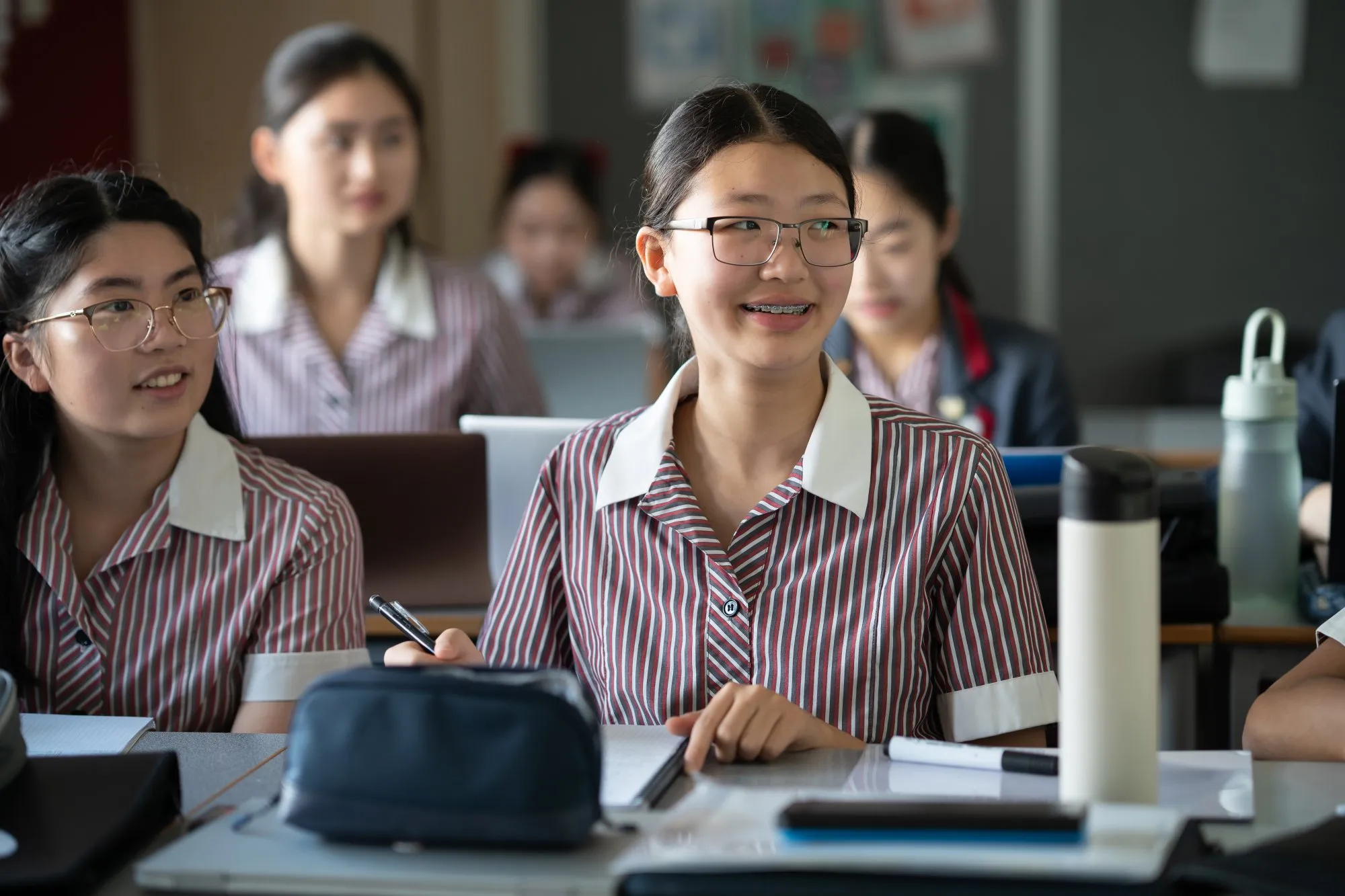 Students in striped school uniforms sitting at desks and smiling in a classroom.
